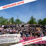 Grote groep mensen met banners en borden blokkeren een brug. In de hoeken staat 'gesteunde actie' en 'het actiefonds' in rode letters op een wit achtergrond.