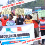 People holding signs that say: "decolonize virunga, climate justice now, free congo" In the corners of the photo it says in red letters on a white background "supported action, Het Actiefonds"