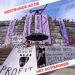 Purple banners stating 'fuck capitalism' and 'fuck airbnb' with in the corners in red on white background 'gesteunde actie' and 'Het Actiefonds