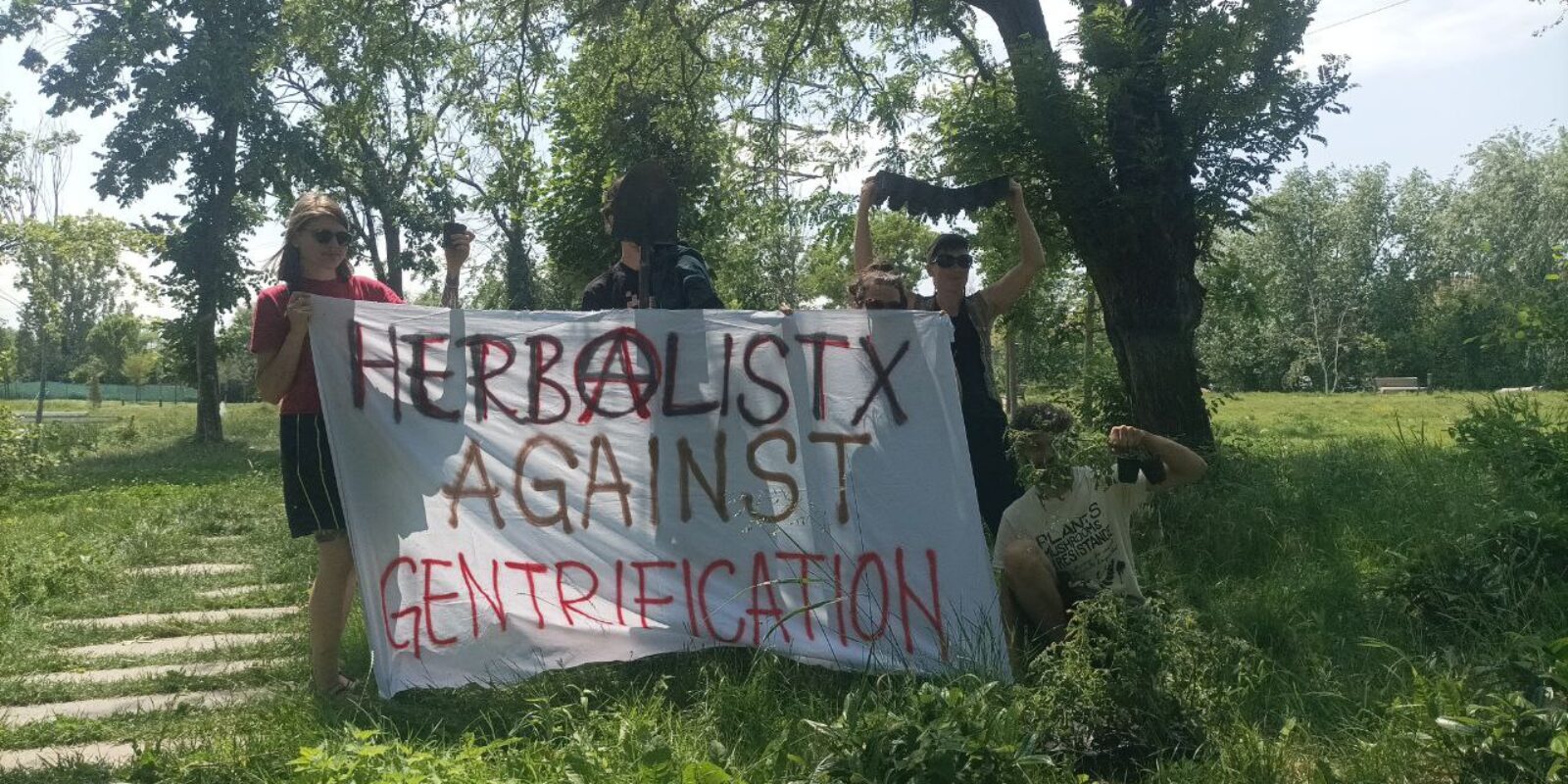 Vier activisten houden een banner omhoog met de tekst 'Herbalists against gentrification'. Ze staan in een bos.